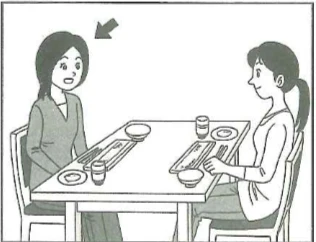 Scene: Two women seated opposite each other at a dining table with meals set. The woman on the left, holding chopsticks and about to eat, has a gray arrow pointing to her — from the JLPT N5 2010–2011 listening section